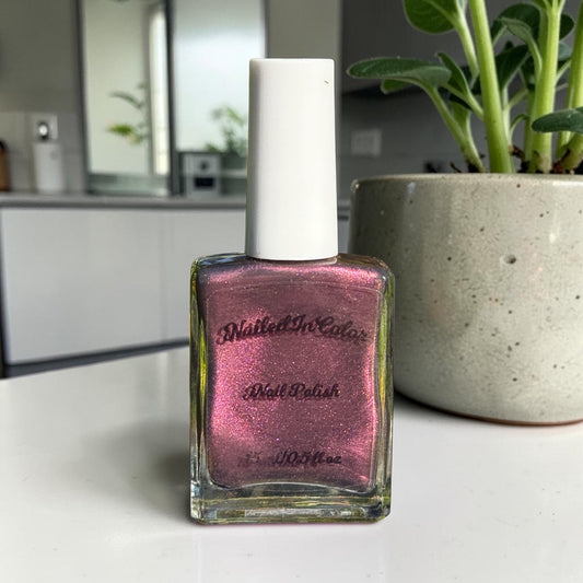 “Dusky Wine deep mulled wine nail polish bottle on a counter with plant in background”