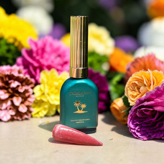 Teal bottle with gold cap on a surface with a polished nail swatch of light red cat eye surrounded by colorful flowers