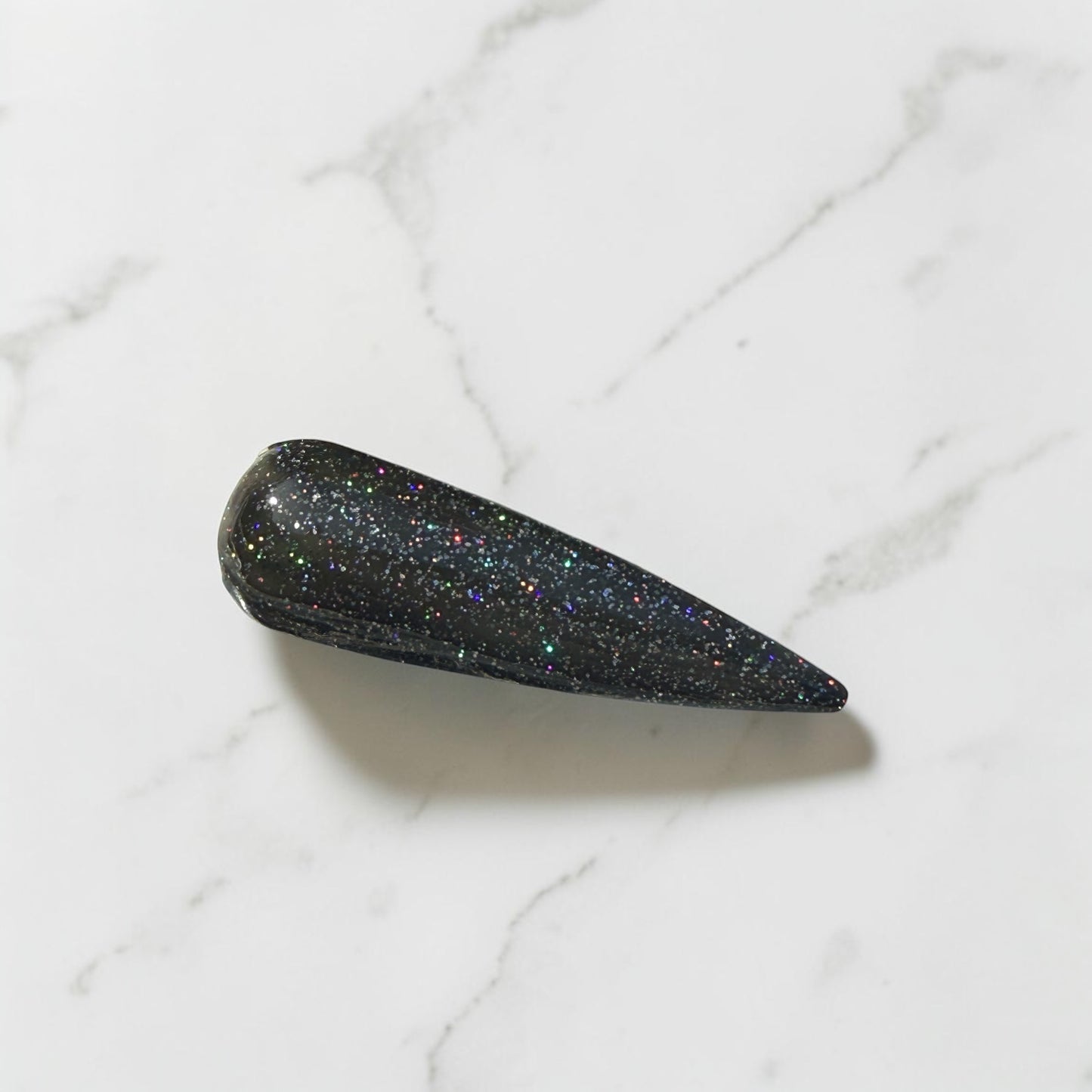 Black glittery nail swatch on a marble surface