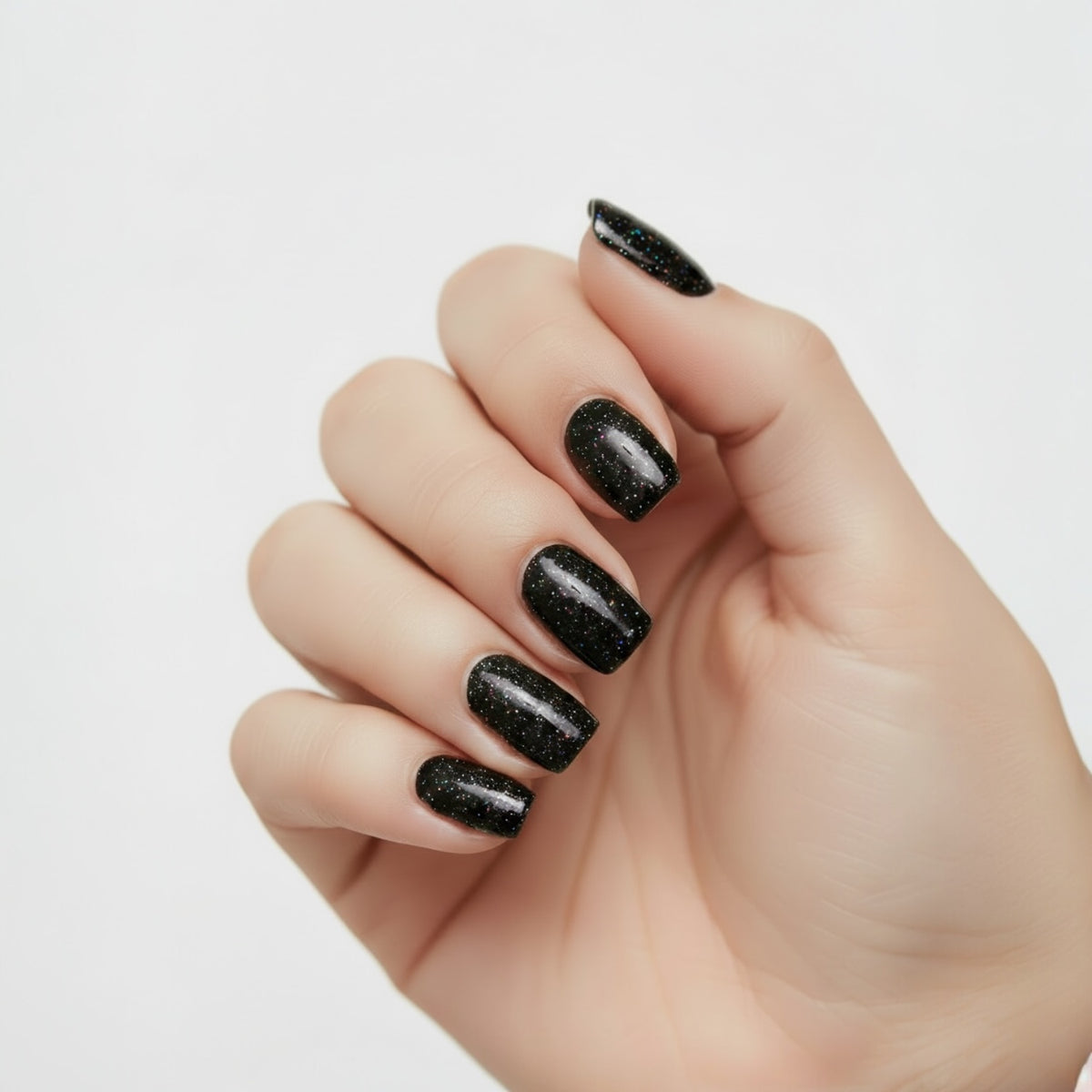 Hand with black holographic glitter nail polish on a light gray background