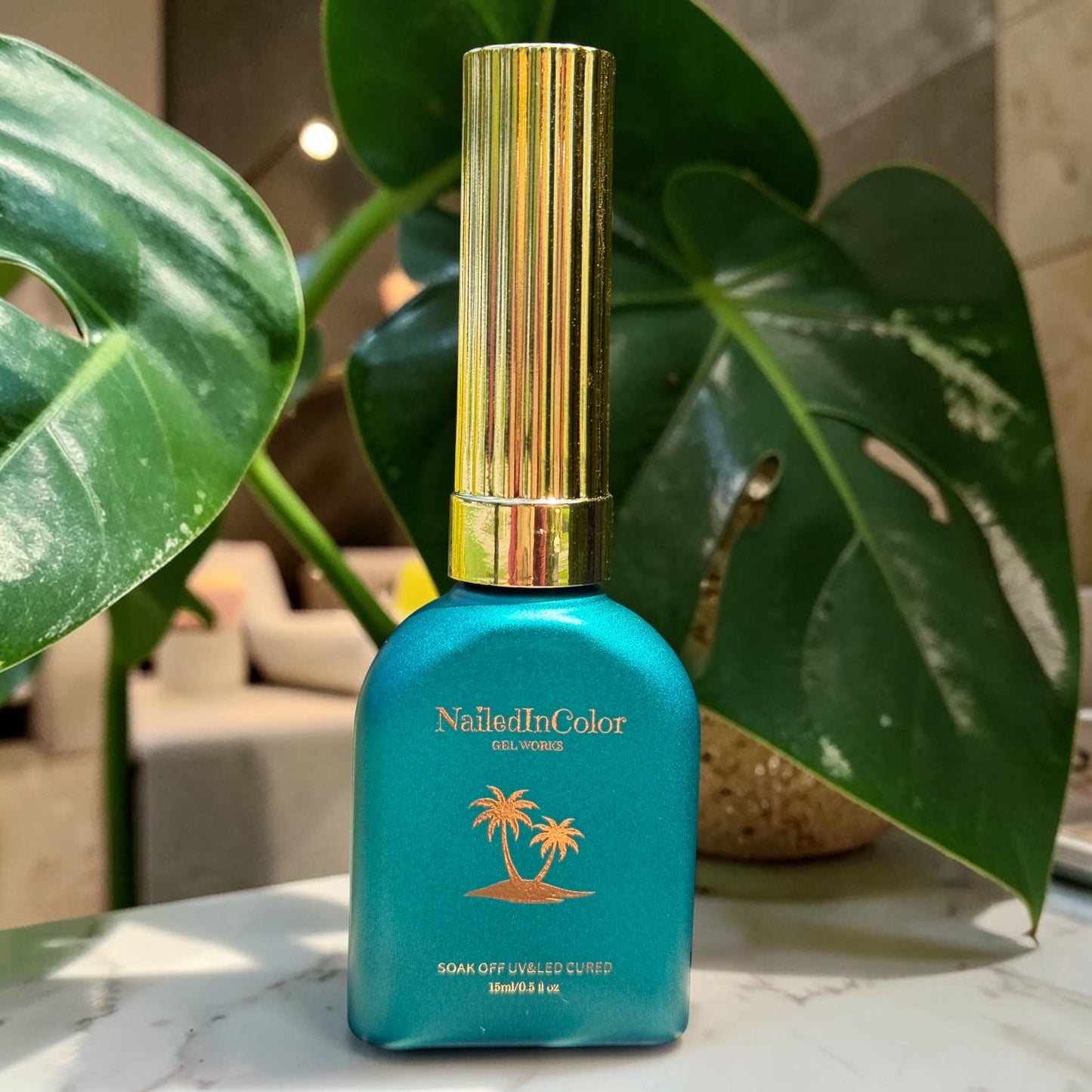 Green nail polish bottle with gold cap on a marble surface with green leaves in the background