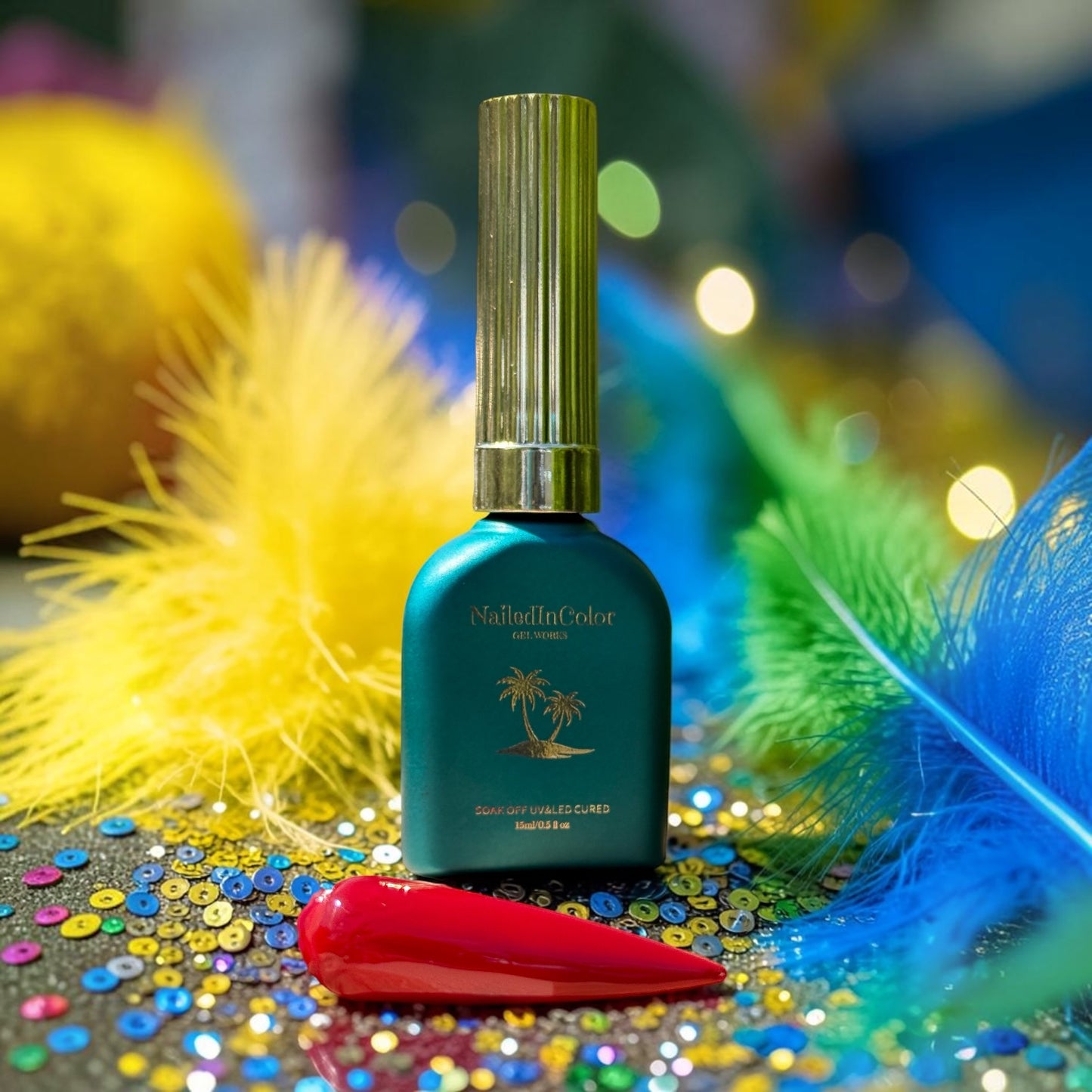 Green nail polish bottle with gold cap on a colorful background with feathers and sequins and a red nail swatch
