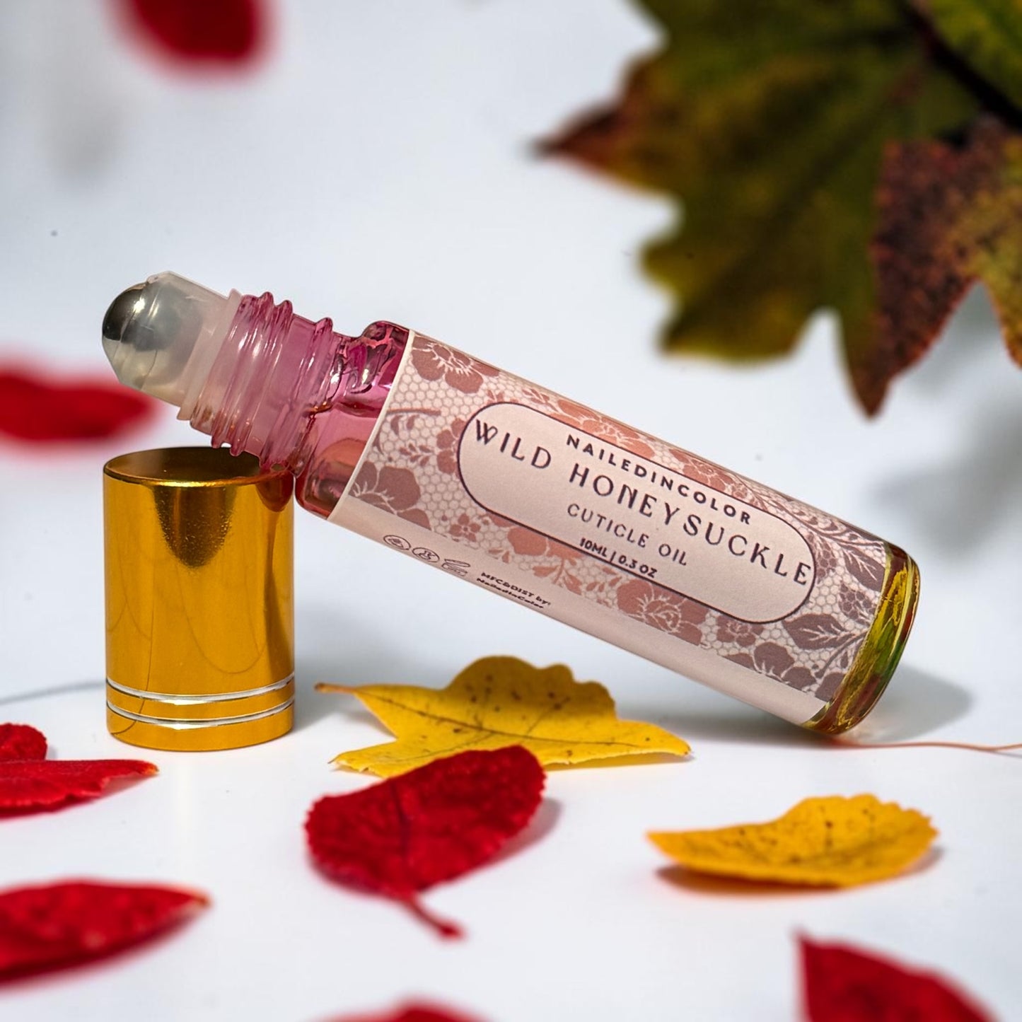 bottle of wild honeysuckle resting on its cap on white counter with yellow and red small leaves