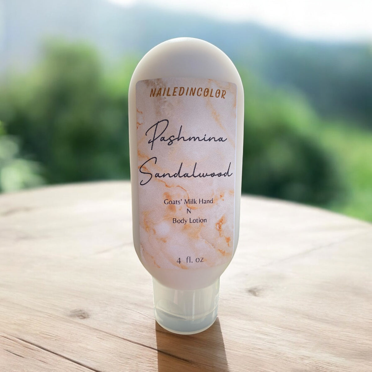 A bottle of Naild in Color Pashmina Sandalwood Cream Milk Hand & Body Lotion stands on a wooden table with a blurred green outdoor background.