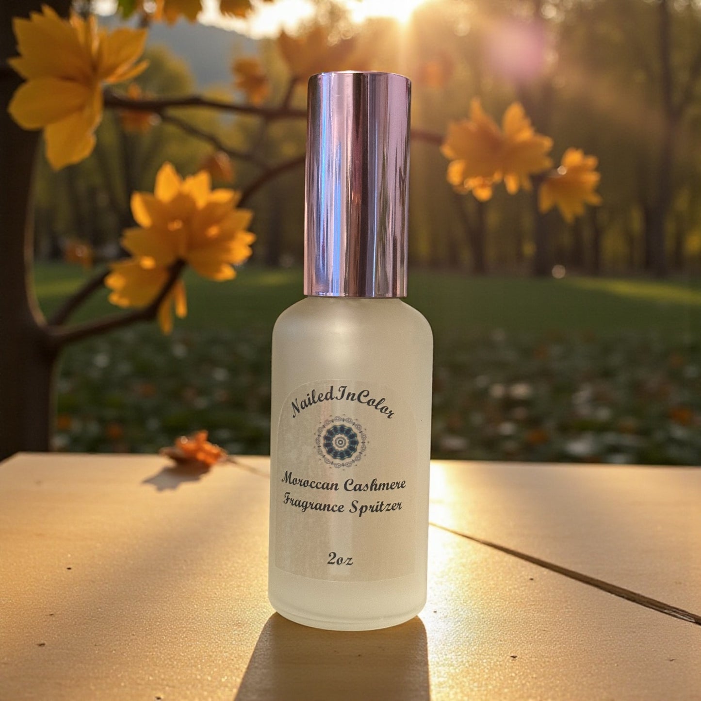 Frosted bottle with rose gold cap labeled 'Nailed In Color' Moroccan Cashmere Fragrance Spritzer on a wooden surface with yellow flowers in the background.