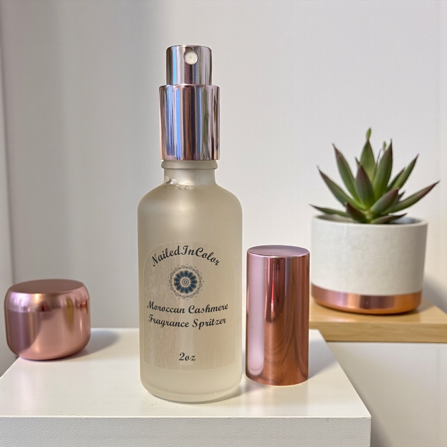 Nailed In Color Moroccan Cashmere Fragrance Spritzer bottle with rose gold cap and base on a white surface with a plant in the background.