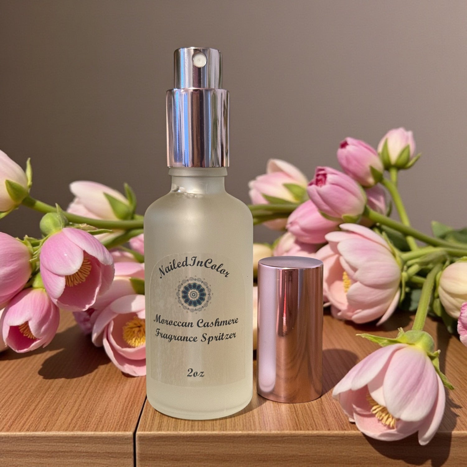 Nailed In Color Moroccan Cashmere Fragrance Spritzer bottle with pink flowers on a wooden surface