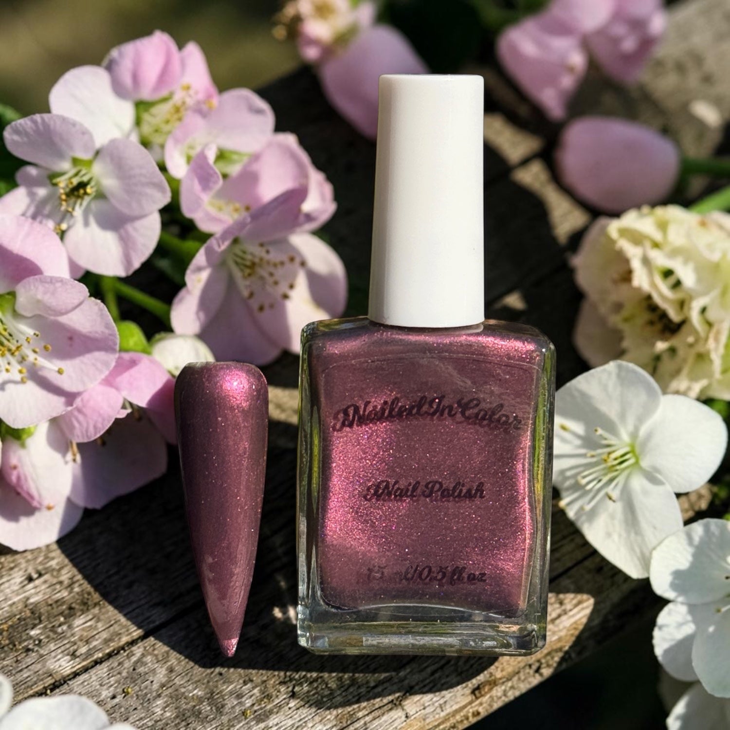 “Dusky Wine deep mulled wine nail polish bottle on a bench with flowers in background”