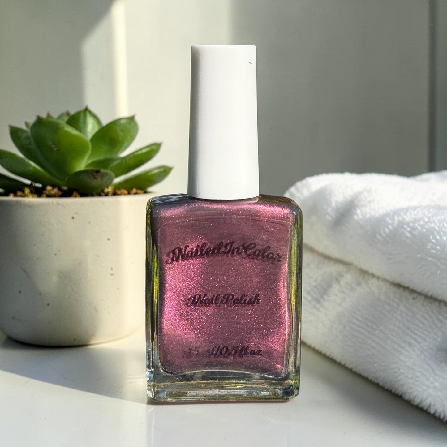 “Dusky Wine deep mulled wine nail polish bottle on a pastel background with plant and towels