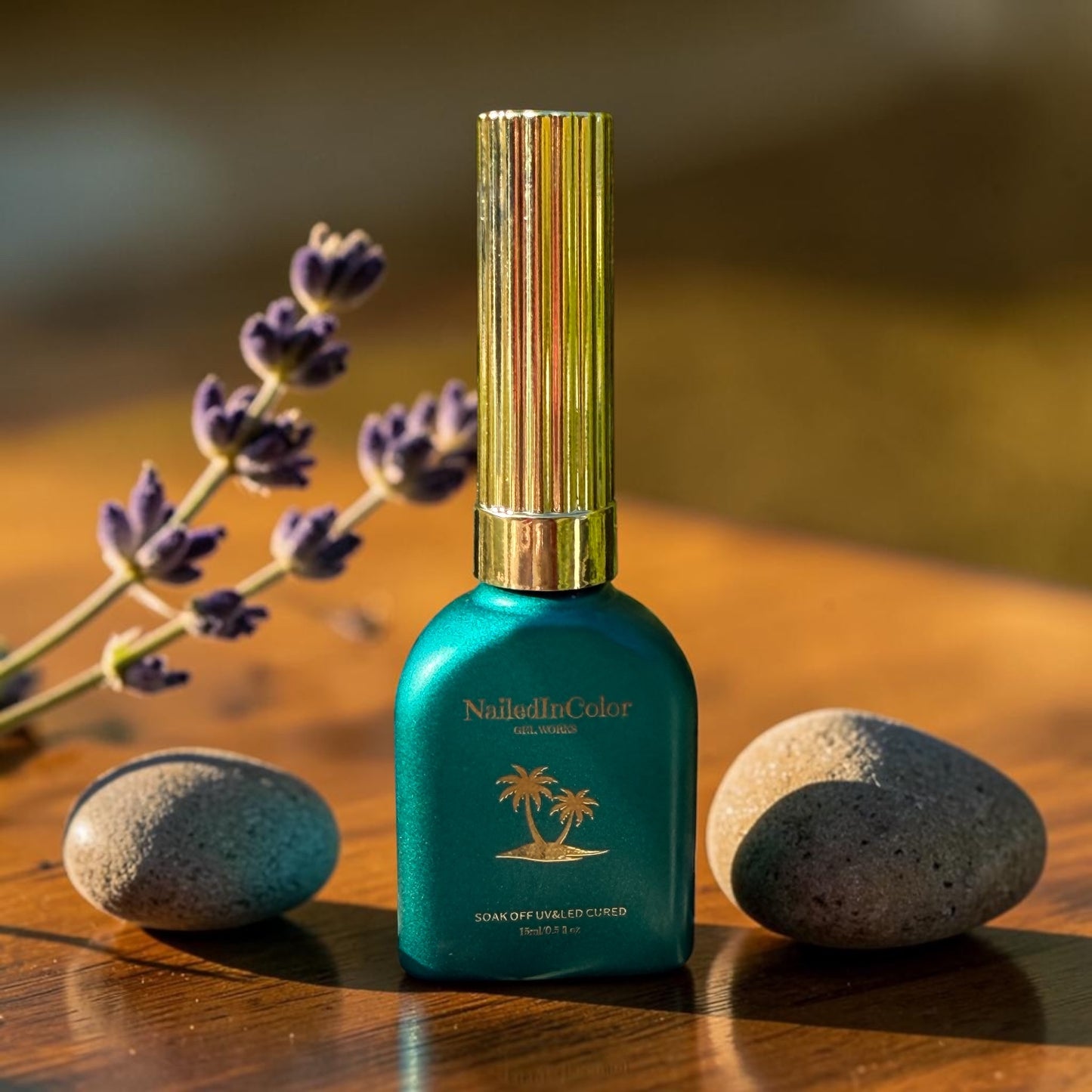 green nail polish bottle with gold cap on a wooden surface with stones and lavender.