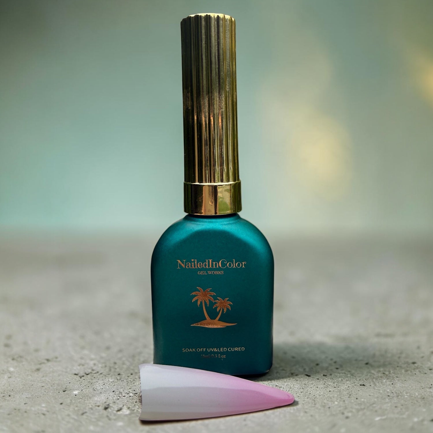 Satin green gel polish bottle with gold cap on a granite top and pale green background. nail swatch of white and pale pink