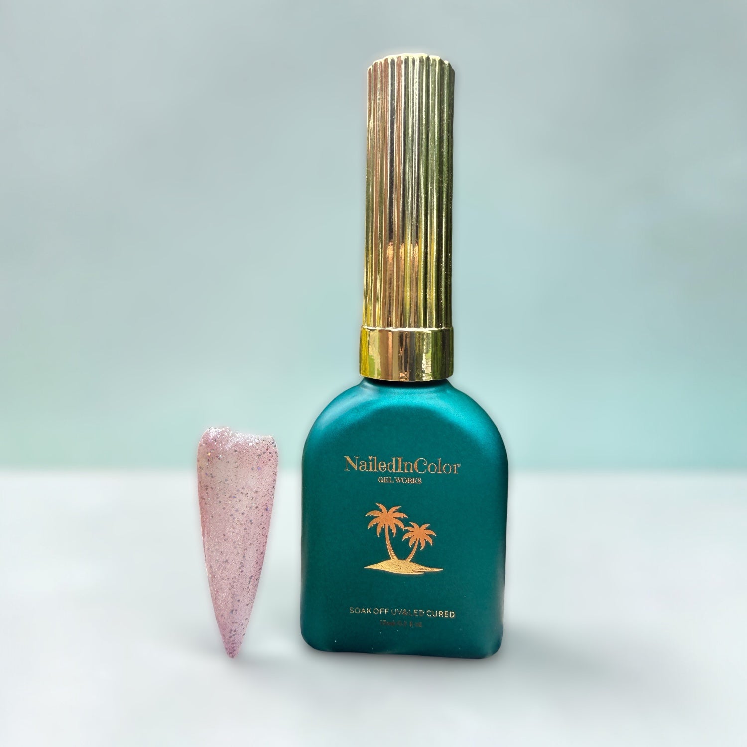 Teal nail polish bottle with gold cap and light lavender glittery nail tip on a light gray background