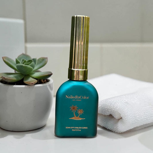 Green NailedInColor gel polish bottle on a counter with a plant and towel.