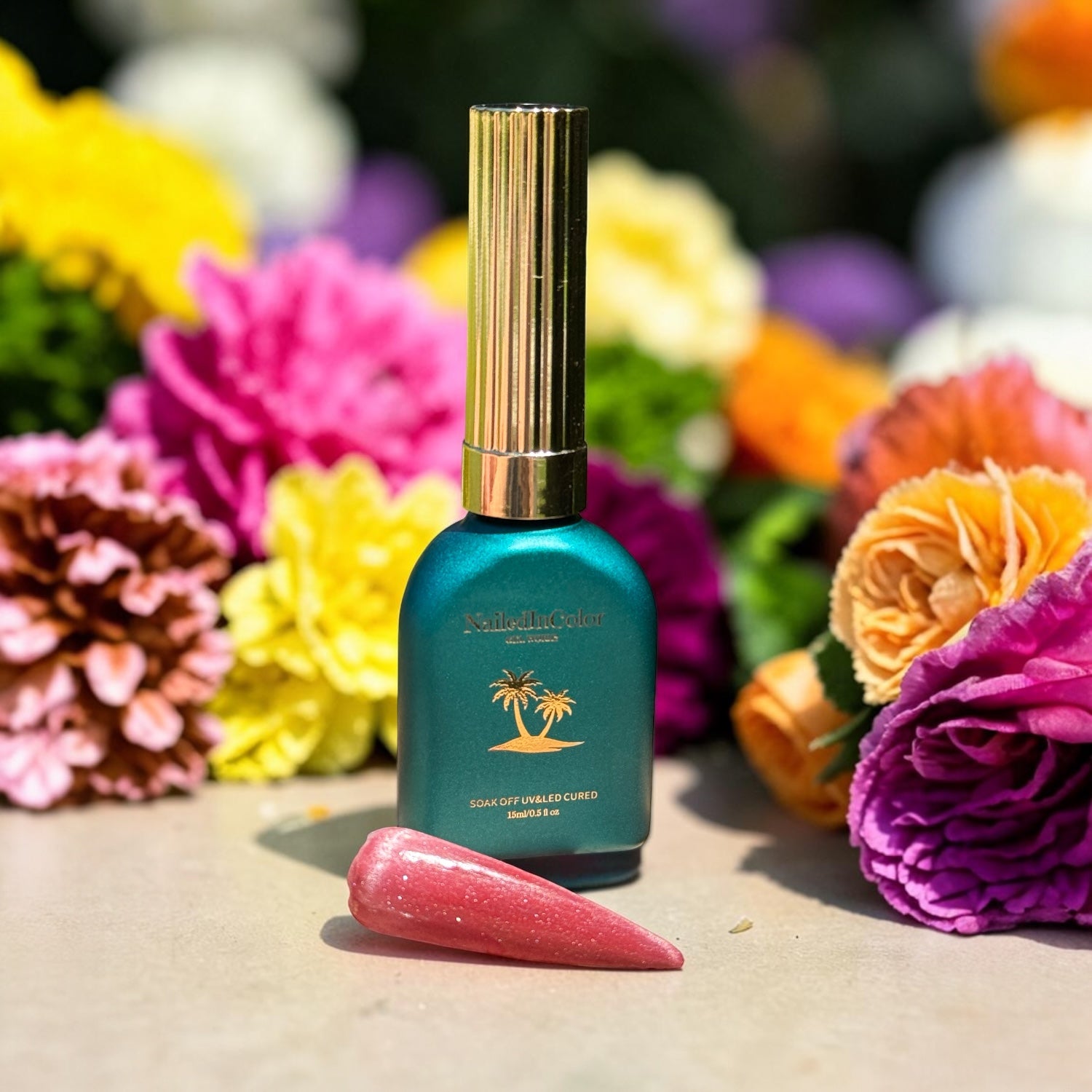 Teal bottle with gold cap on a surface  with a polished nail swatch of light red cat eye surrounded by colorful flowers