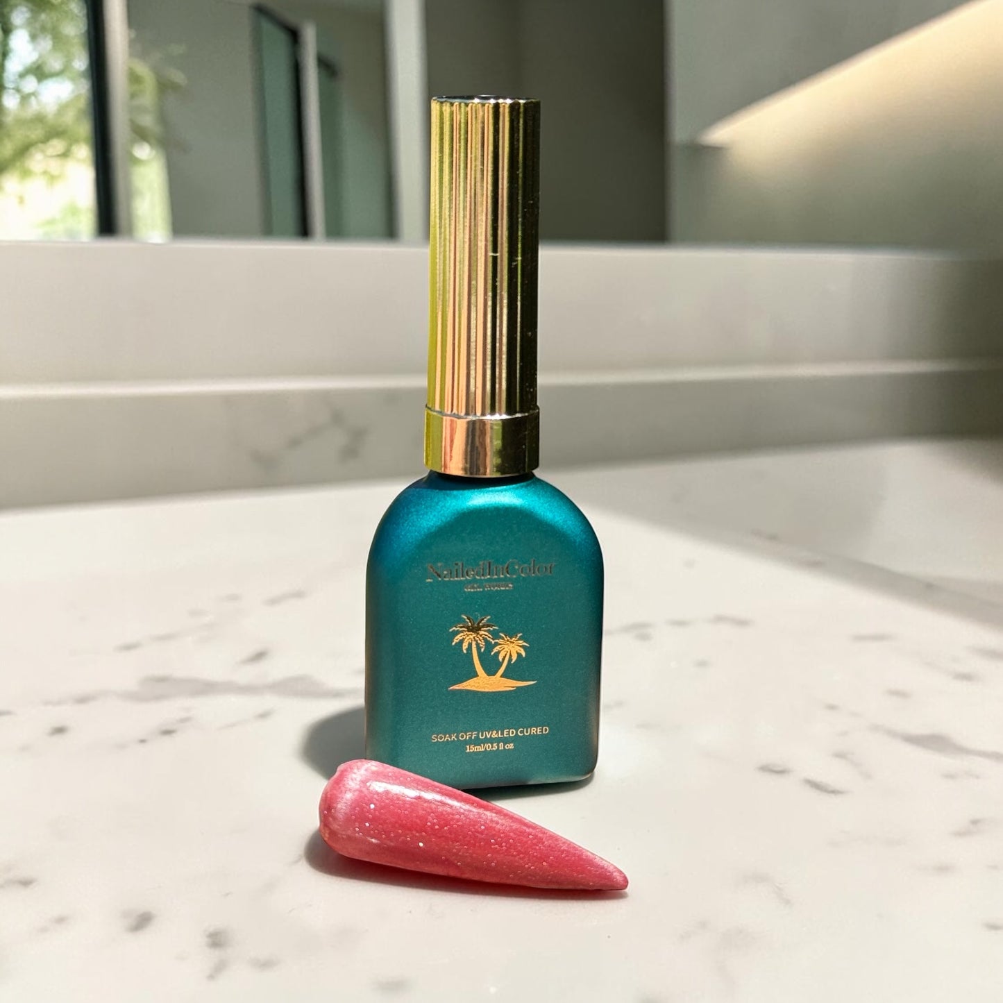 Teal bottle with gold cap on a marble surface and a light red cat eye nail swatch