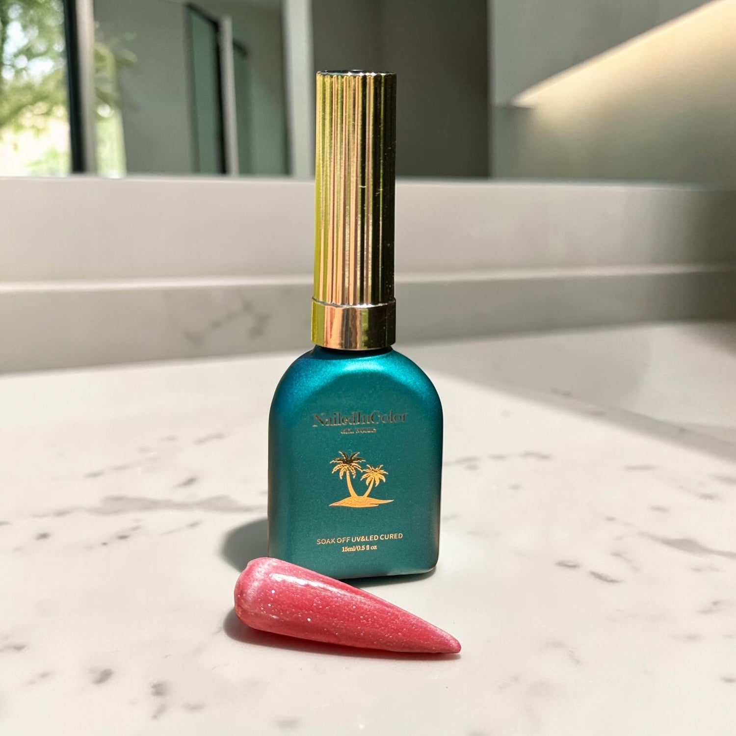 Teal bottle with gold cap on a marble surface and a light red cat eye nail swatch
