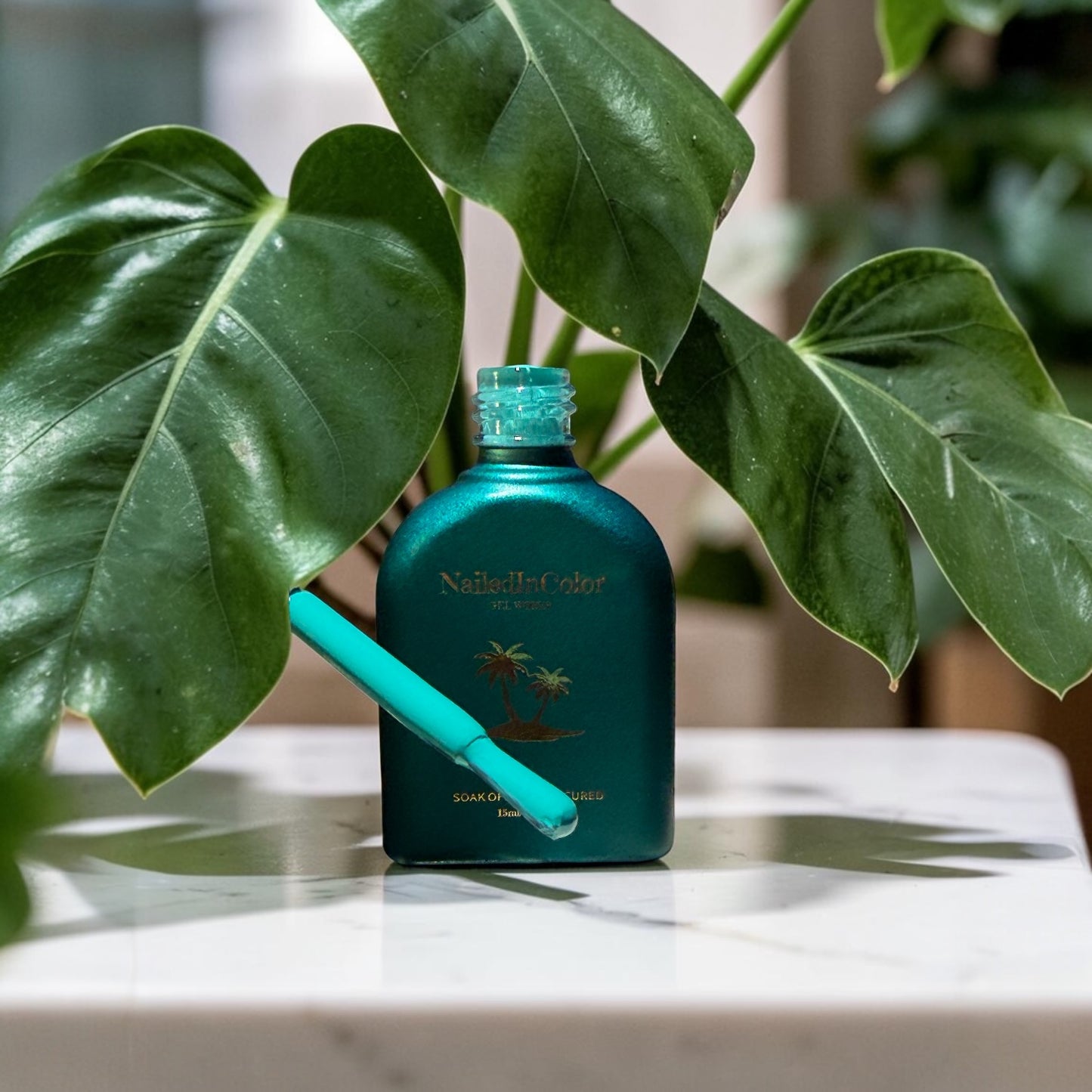 A green gel polish bottle with a polish brush dipped in blue green color in front of large plant leaves