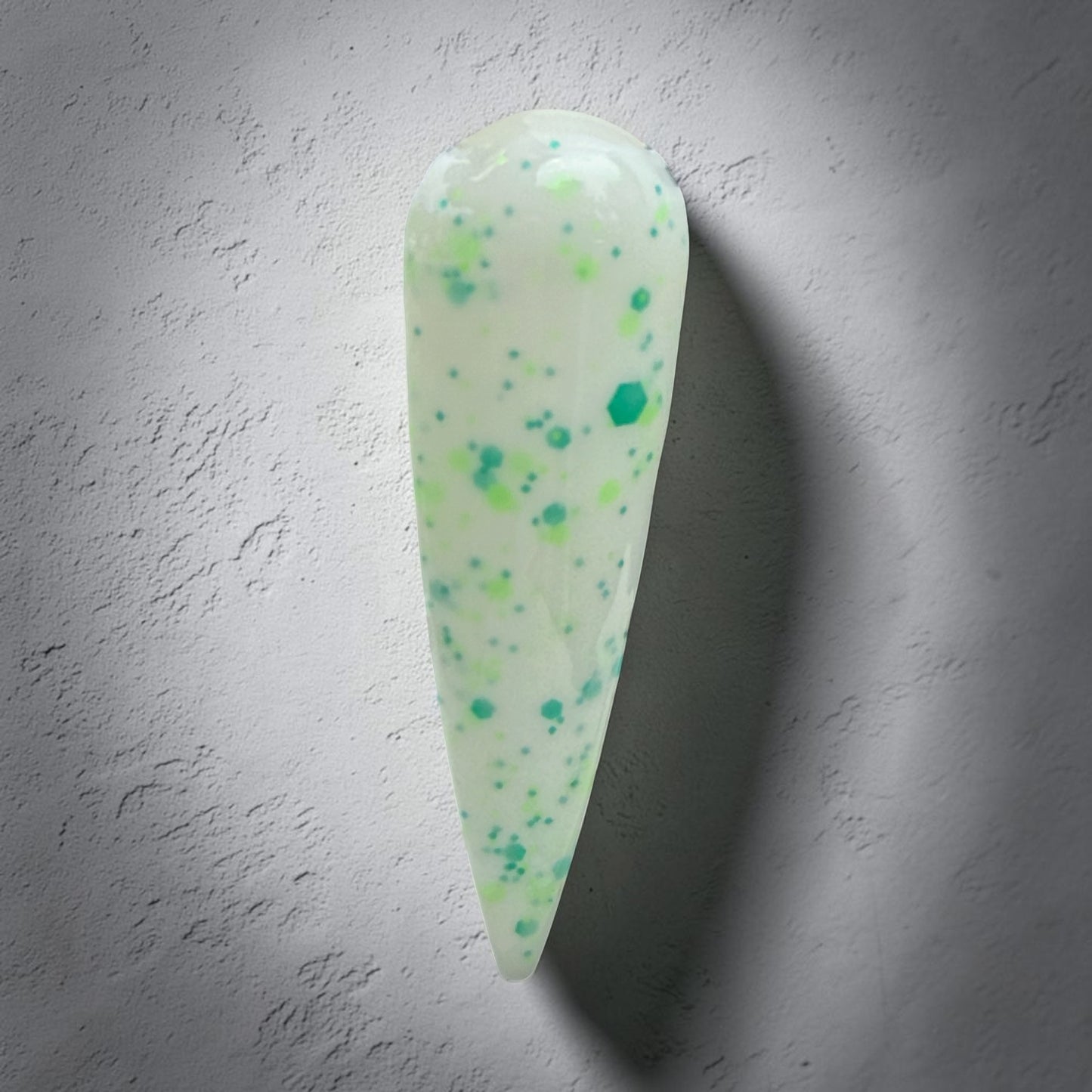 Green and white speckled nail swatch highlighted on a gray background