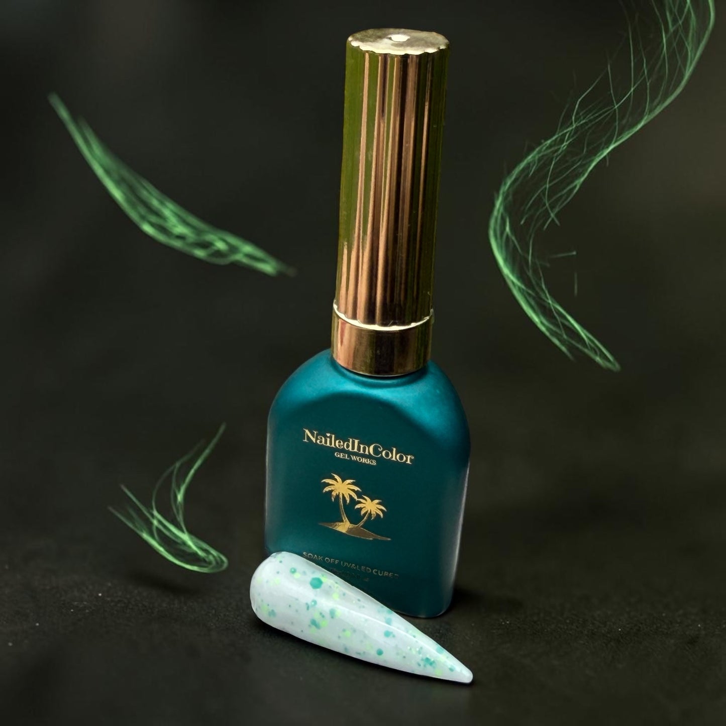 NailedInColor gel polish bottle with a gold cap, polish green and cream speckled nail swatch in front, small wisps of geen like fog and a dark gray background