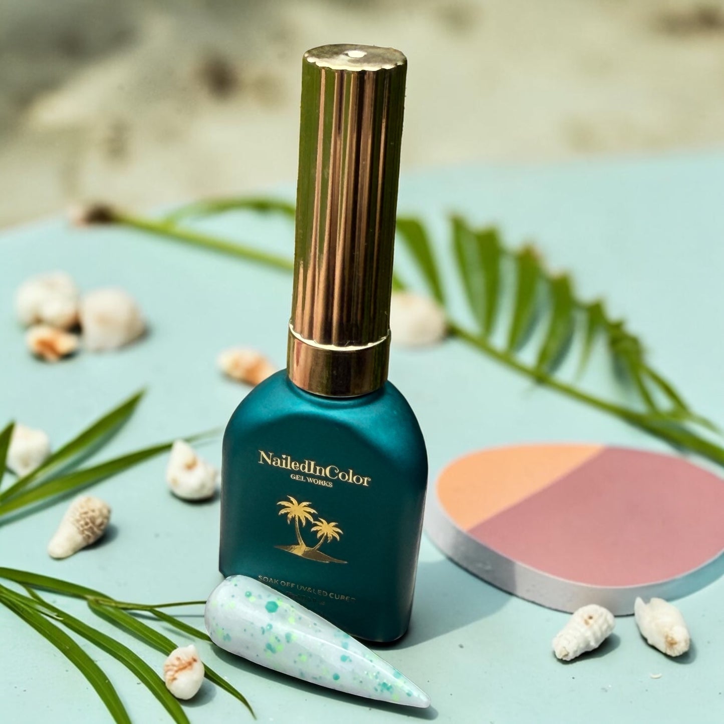 NailedInColor nail polish bottle on a beach-themed background with a polished nail swatch and palm leaves and shells.