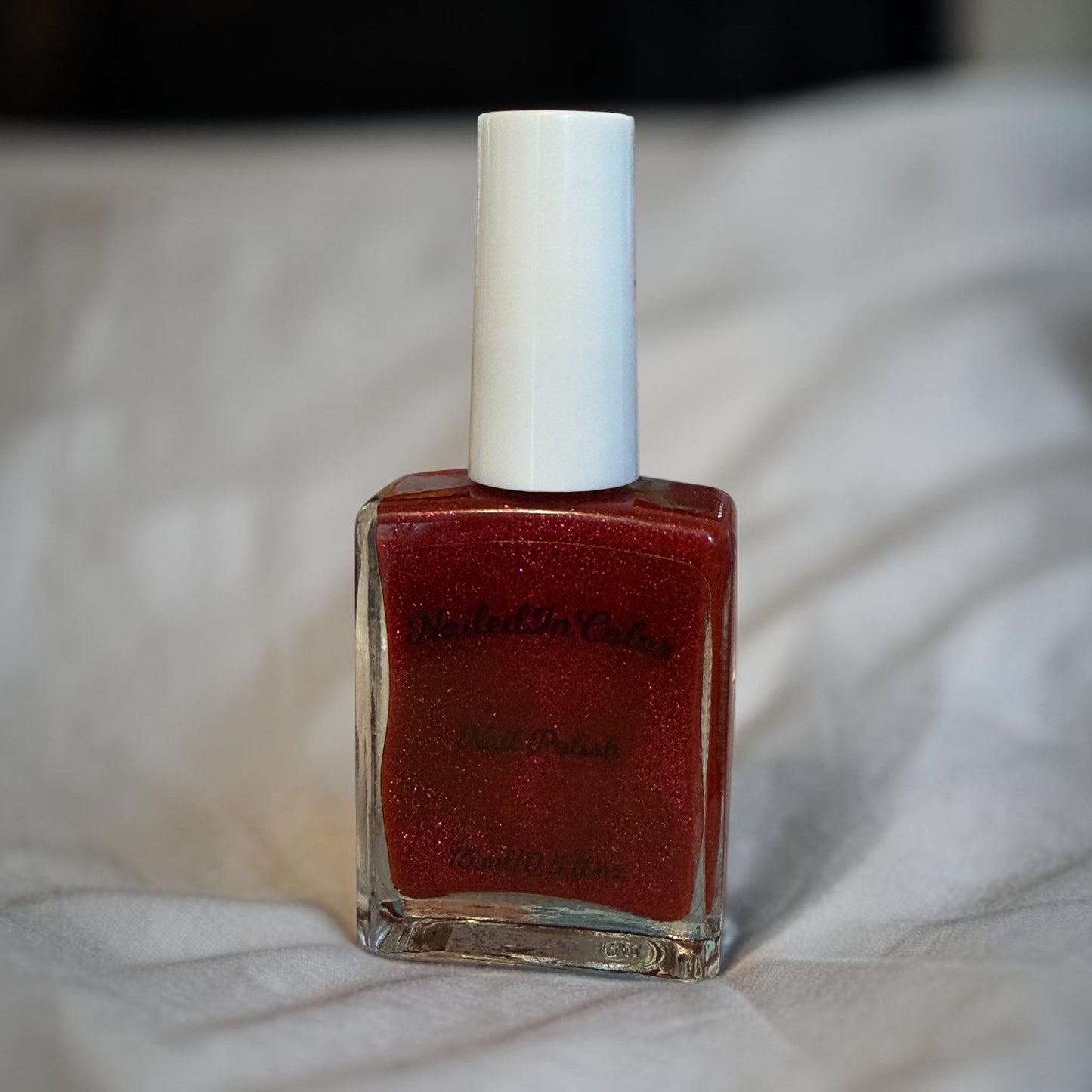 Red nail polish bottle with white cap on a light fabric background