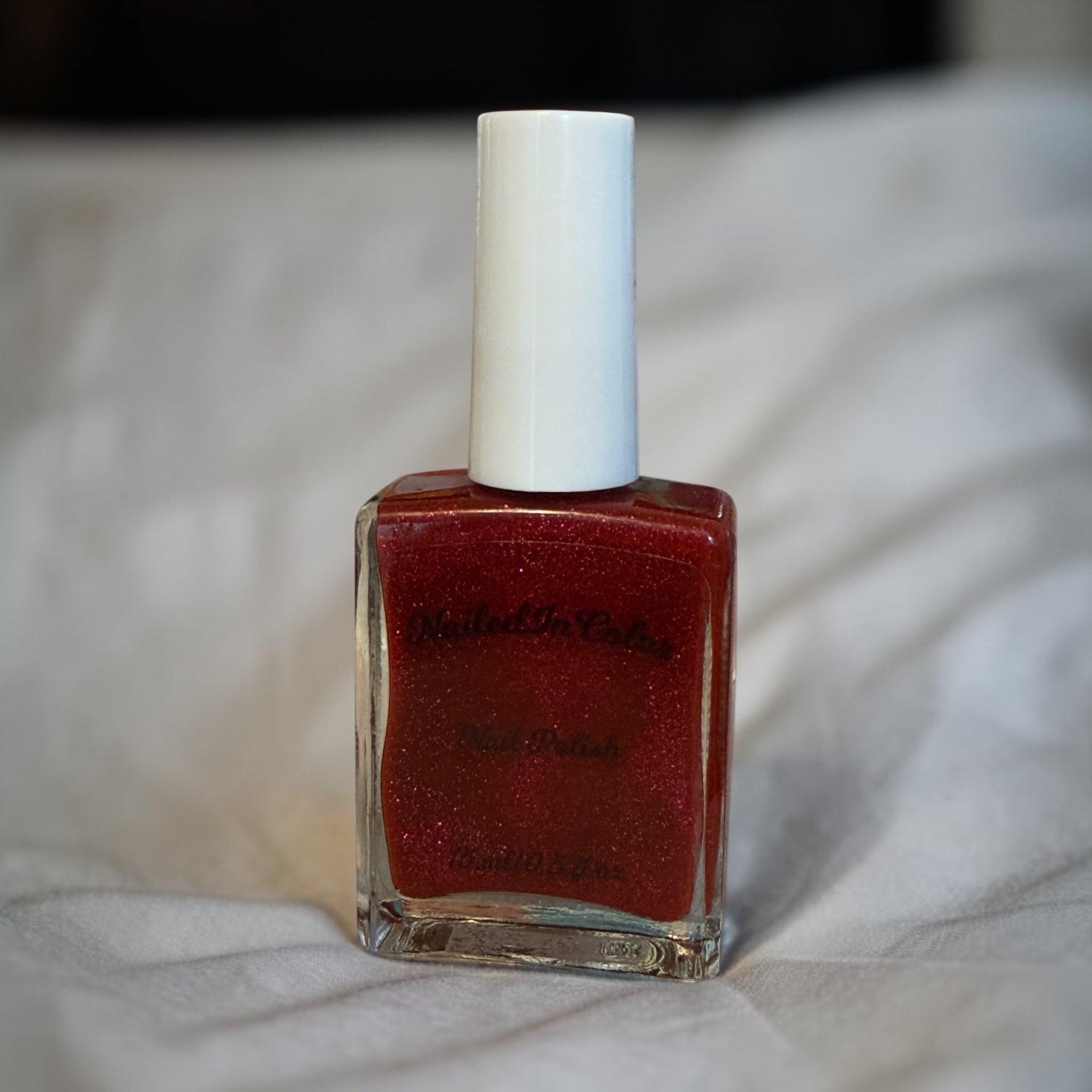 Red nail polish bottle with white cap on a light fabric background