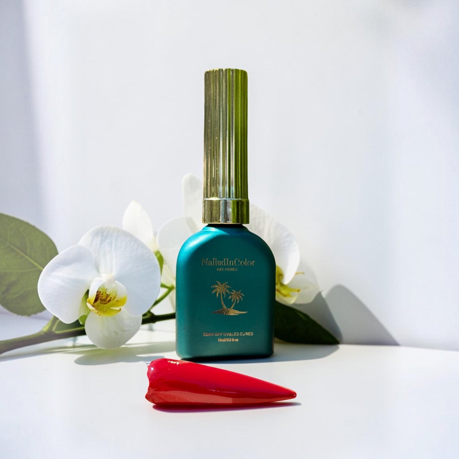 Teal bottle with gold cap on a white surface with white flowers and a red nail swatch.