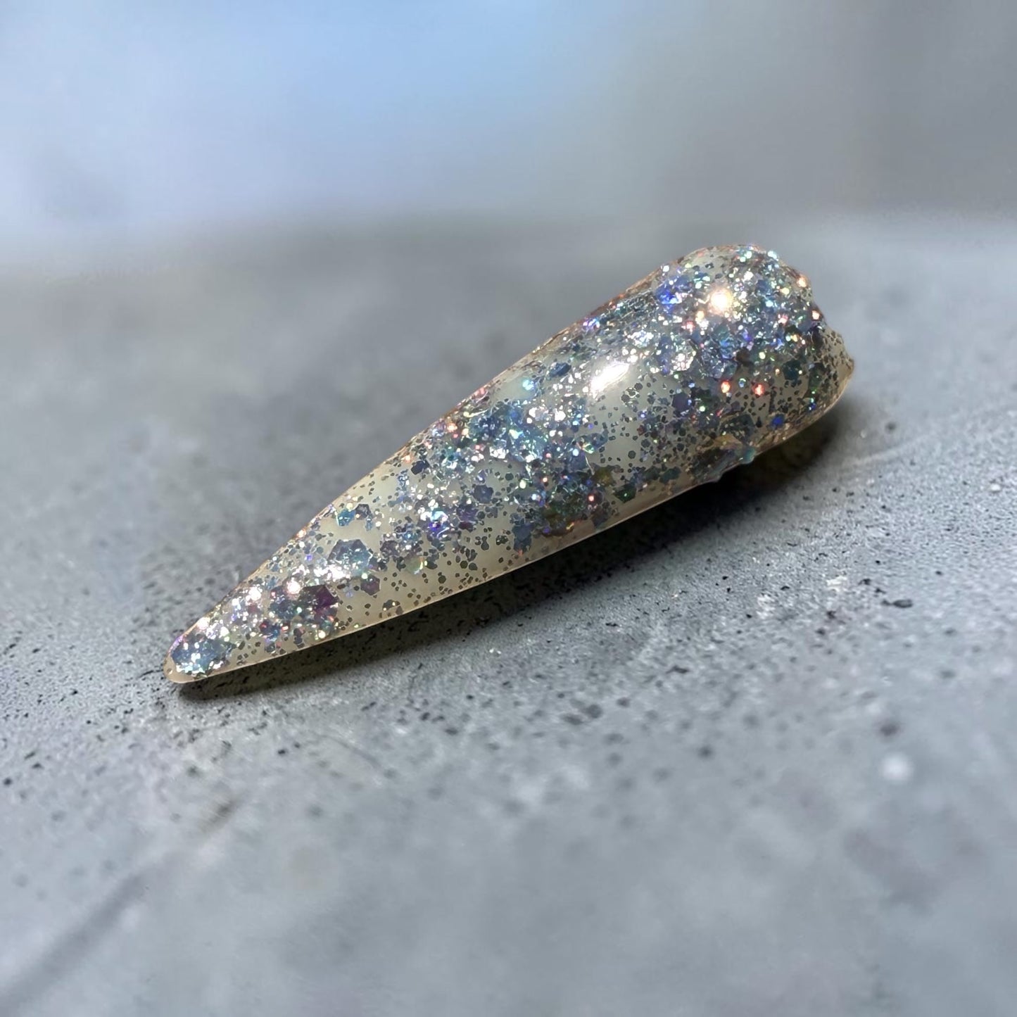 Glittery silver nail tip on a gray surface