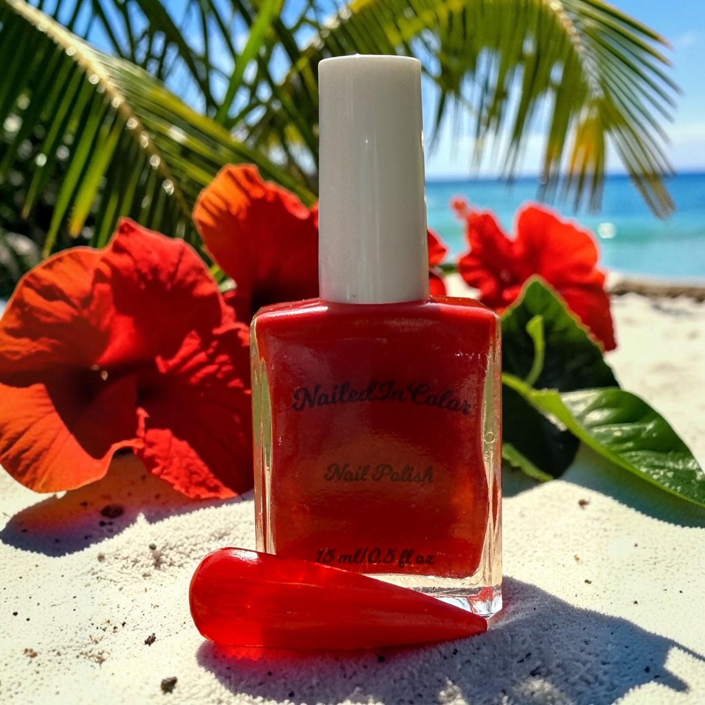 coral orange nail polish bottle with a nail tip on a sandy beach with flowers and palm leaves in the background
