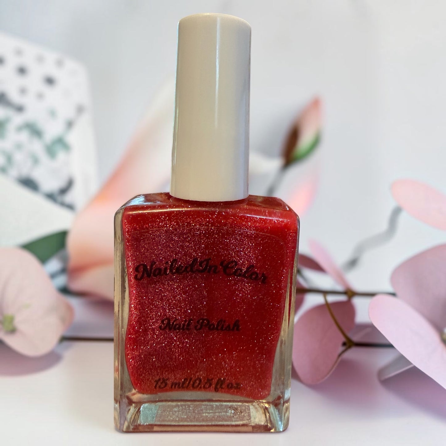 Deep dark pink glittery nail polish bottle with a blurred floral background