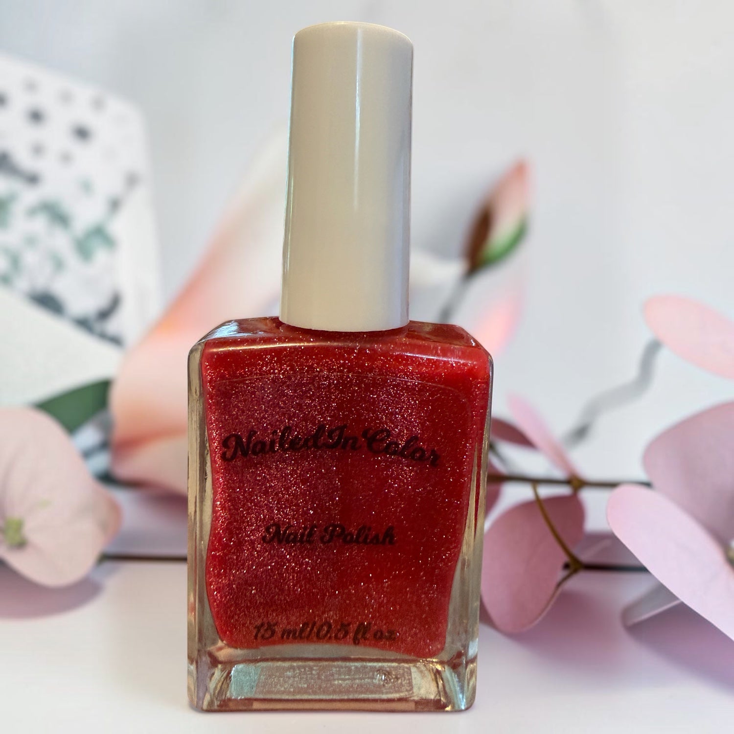 Deep dark pink glittery nail polish bottle with a blurred floral background