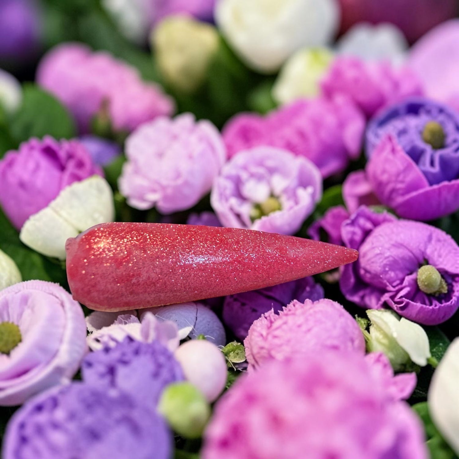 Pink glitter nail tip on a bed of purple and white flowers