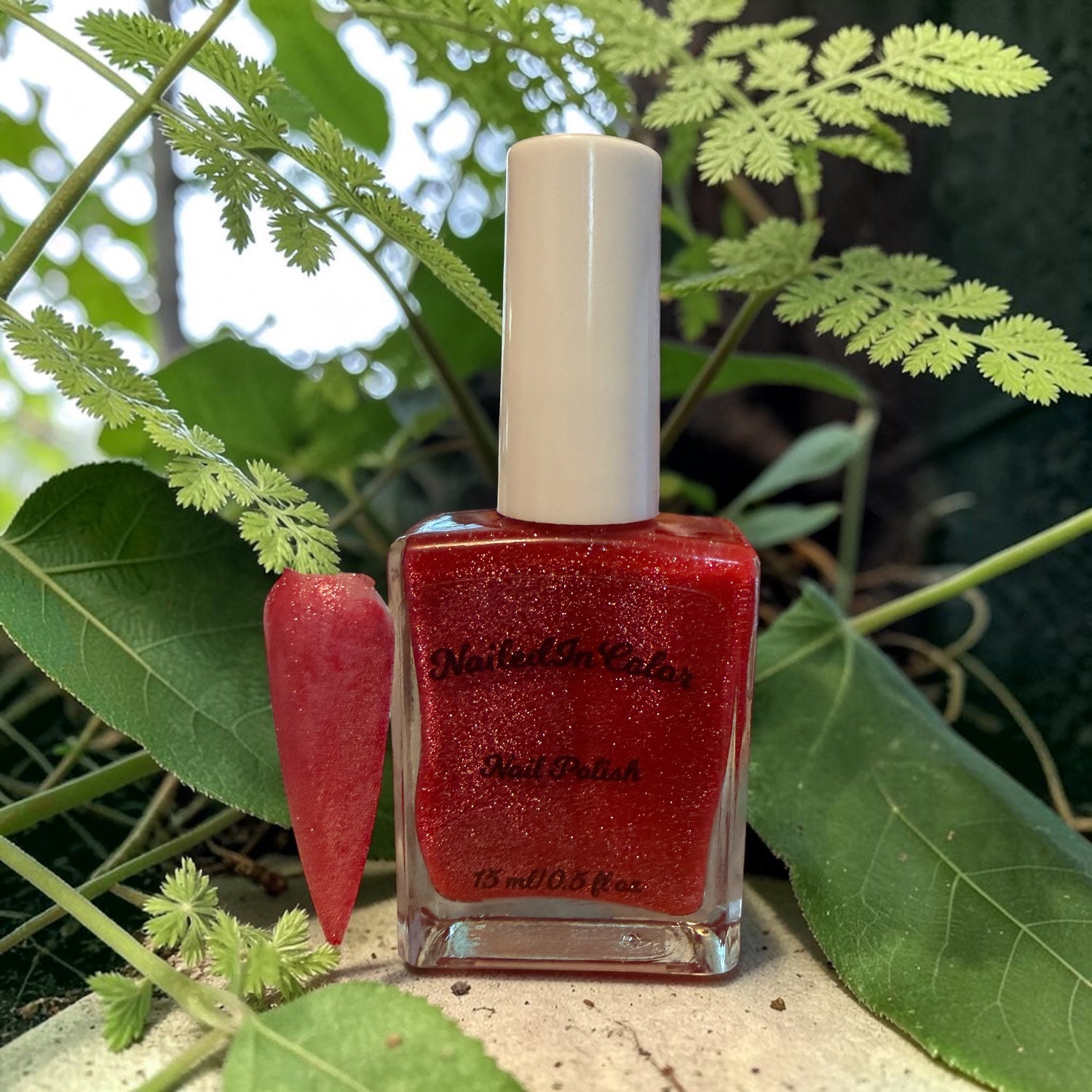 Pink nail tip with polish bottle with a white cap on a natural background with green leaves.
