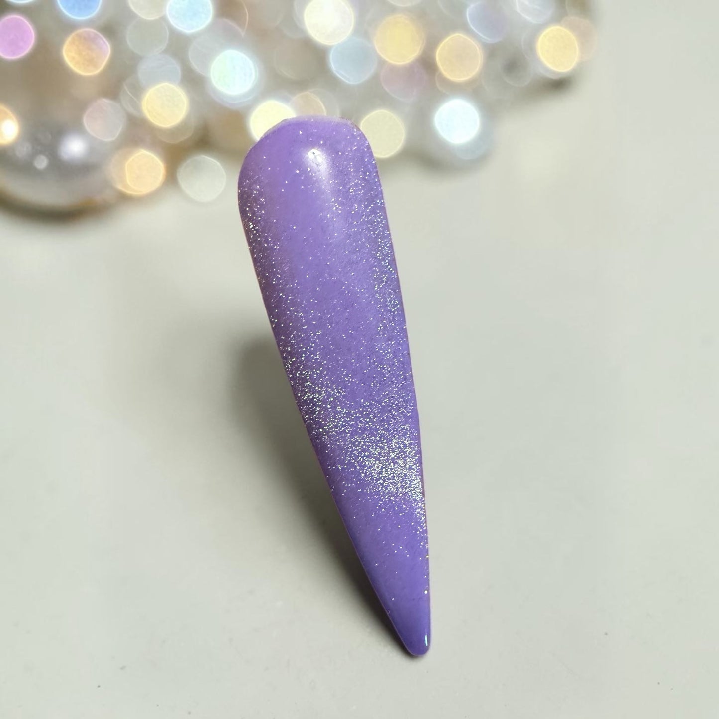 Purple nail tip with silver cat eye topcoat on a light background with blurred lights in the corner