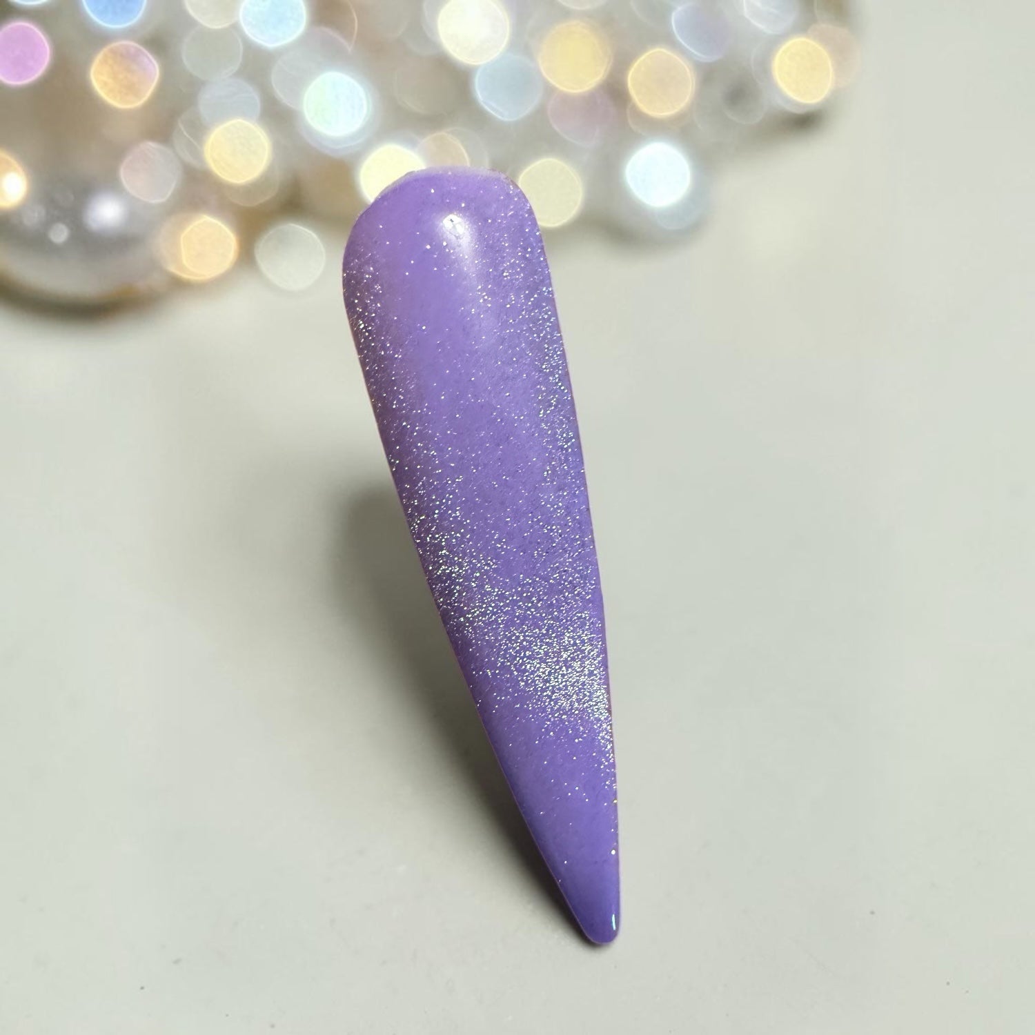 Purple nail tip with silver cat eye topcoat on a light background with blurred lights in the corner