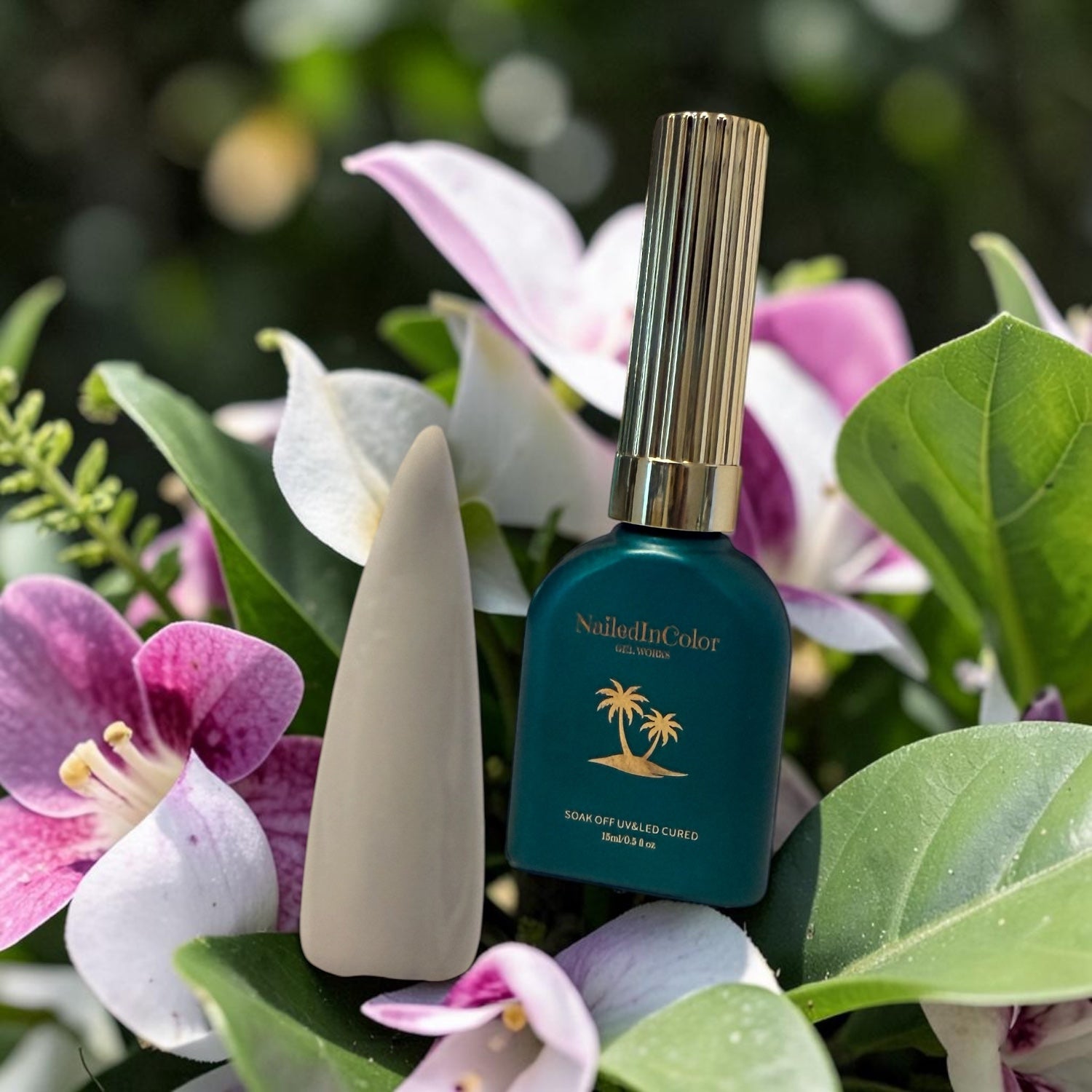 white nail tip resting against flowers with a green polish bottle with a gold cap