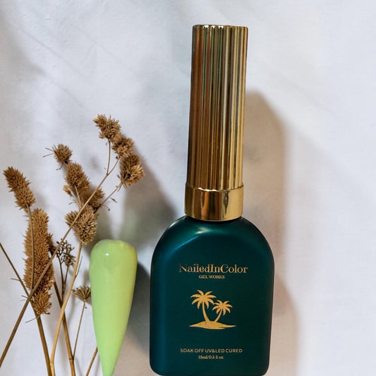 Yellow nail tip with brown florals next to a green polish bottle with a gold cap and soft gray background