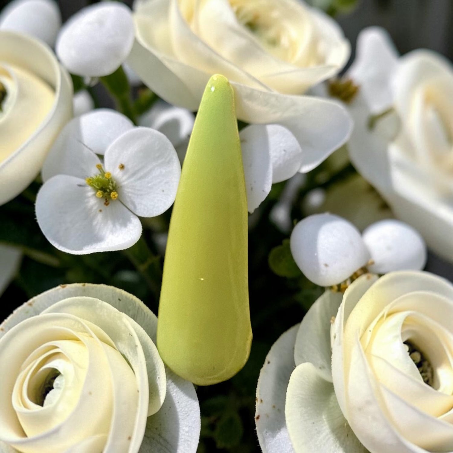 Yellow polished nail tip resting on white florals