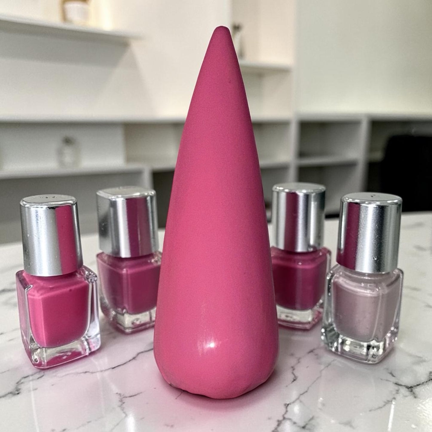 pink nail tip on marble counter surrounded by nail polish bottles and shelves in background