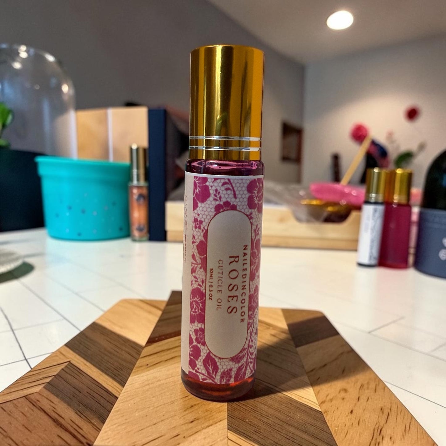 A bottle of Roses cuticle oil with a shiny gold cap and a pink floral label, standing on a wooden cutting board in a salon setting.