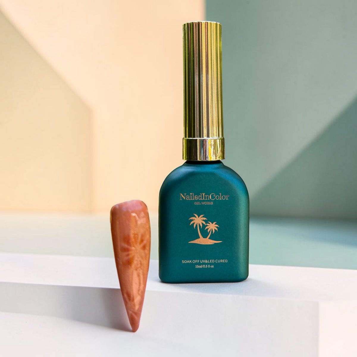 brown nail swatch cat eye effect with teal green polish bottle next to it. Gold lettering and palm tree and pastel green and yellow shade background