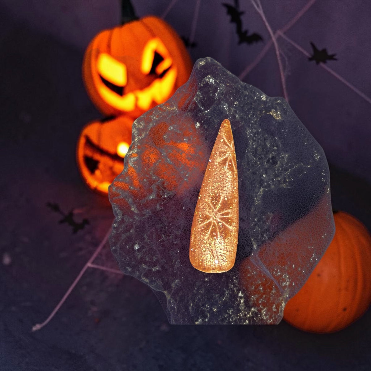 Fall color nail swatch with cat eye design on a web design and jack-o-lanterns and bats in smokey dark background