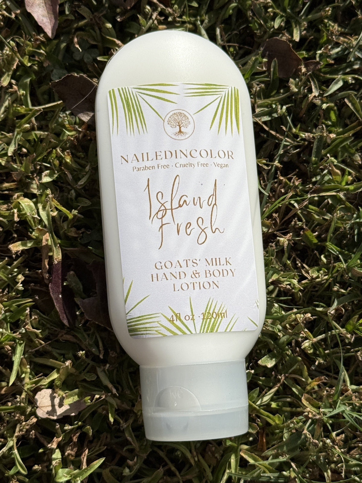 A bottle of NailedinColor 'Island Fresh' hand and body lotion lying on green grass outdoors.