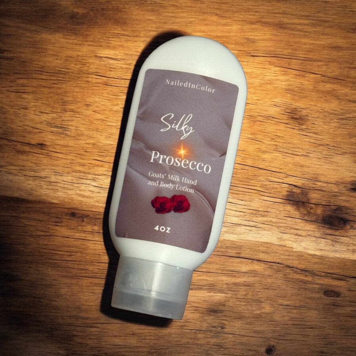 A 4 oz bottle of NailedInColor Silky Prosecco Goats' Milk Hand and Body Lotion, featuring a white squeeze bottle with a brown label and a clear cap, resting on a wooden surface.